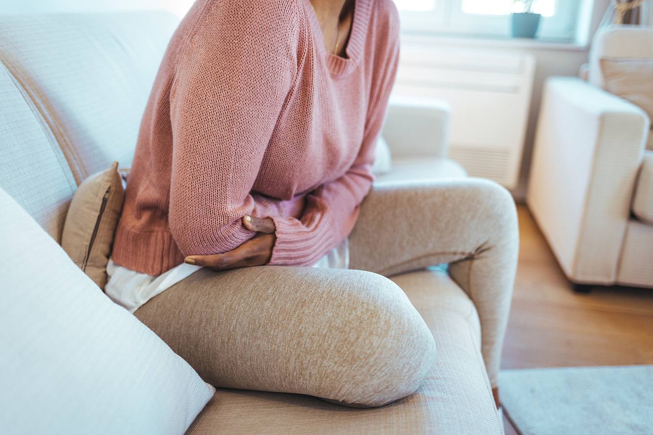 Eine Frau sitzt mit Bauchschmerzen nach Alkohol auf dem Sofa