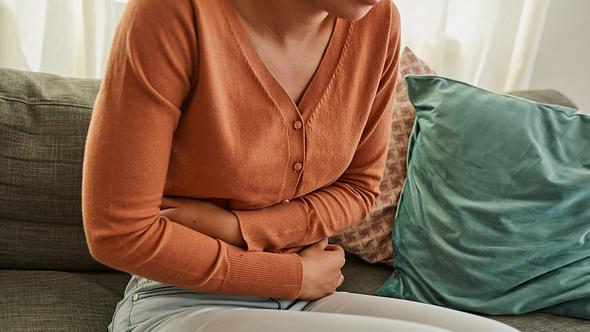 Eine Frau mit Bauchschmerzen nach dem Essen auf dem Sofa - Foto: iStock_LaylaBird