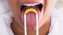 Eine Person reinigt ihre Zunge. - Foto: iStock/AndreyPopov