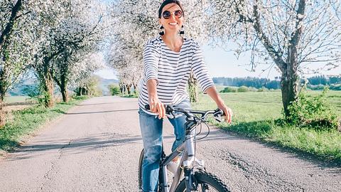 Frau mit Sonnenbrille sitzt auf dem Fahrrad - Foto: Solovyova/iStock