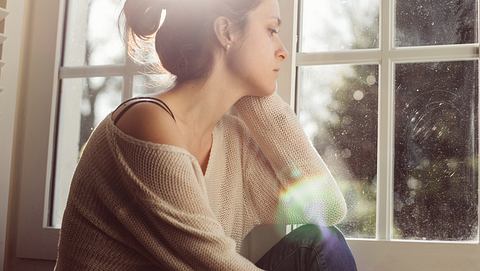 Eine Frau schaut traurig aus dem Fenster - Foto: iStock/Martin Dimitrov