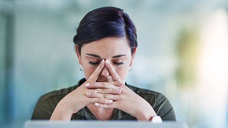 Eine erschöpfte Frau sitzt vor dem Computer und stützt den Kopf auf die Hände - Foto: iStock/LaylaBird