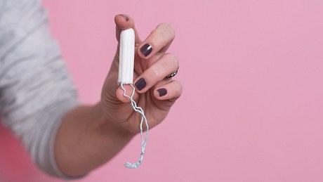 Frau hält Tampon auf lila Hintergrund - Foto: iStock/emapoket
