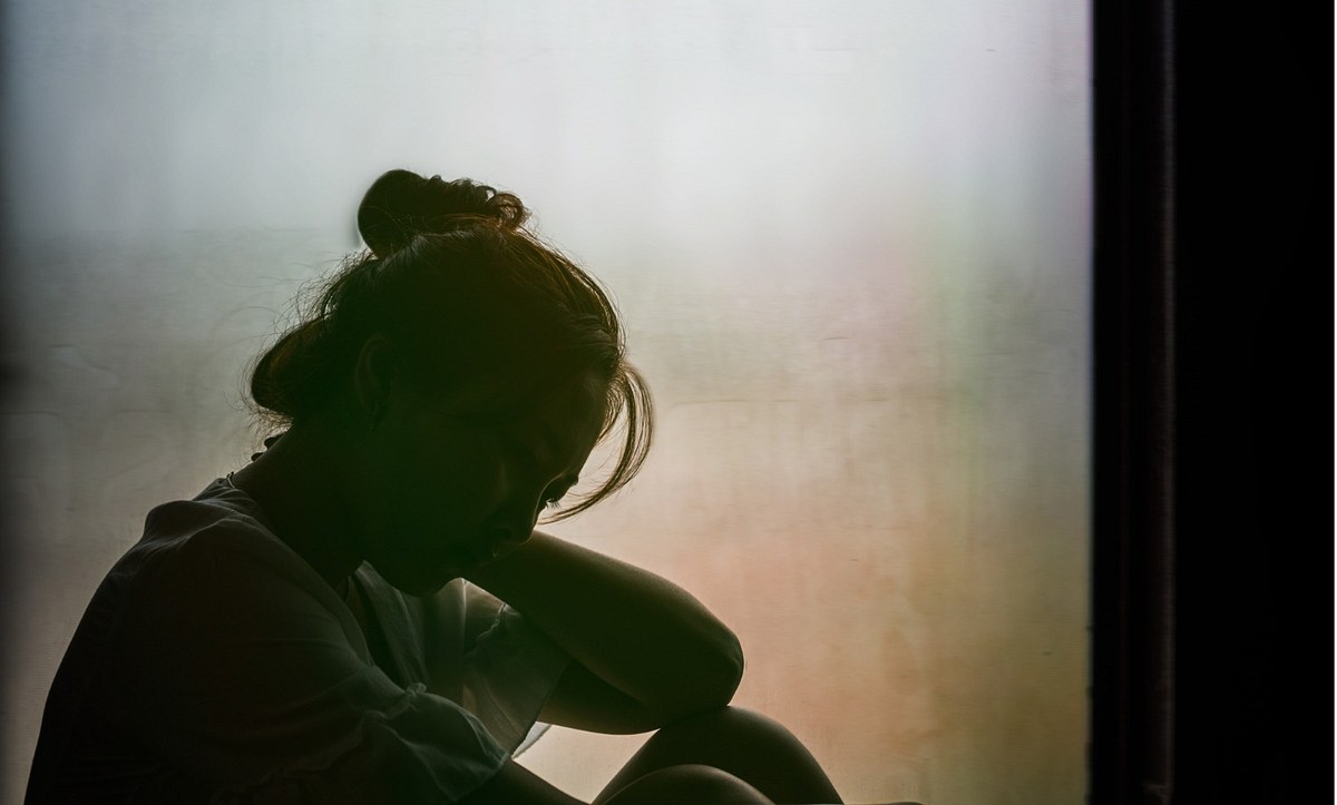 Eine Frau sitzt im Dunkeln mit gesenktem Kopf am Fenster