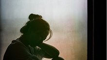 Eine Frau sitzt im Dunkeln mit gesenktem Kopf am Fenster - Foto: istock_kaipong