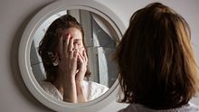 Eine Frau schaut in einen zerbrochenen Spiegel und bedeckt mir beiden Händen ihr Gesicht.  - Foto: iStock/triocean