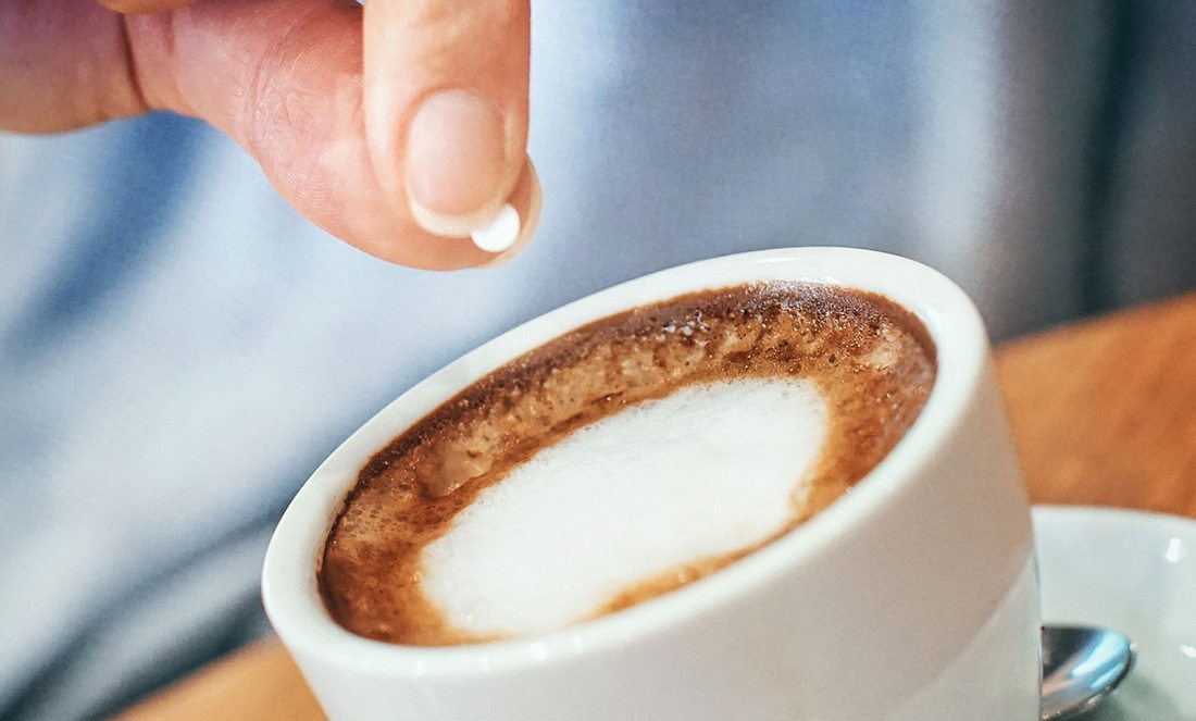 Eine Person wirft ein Stück Süßstoff in eine Kaffeetasse