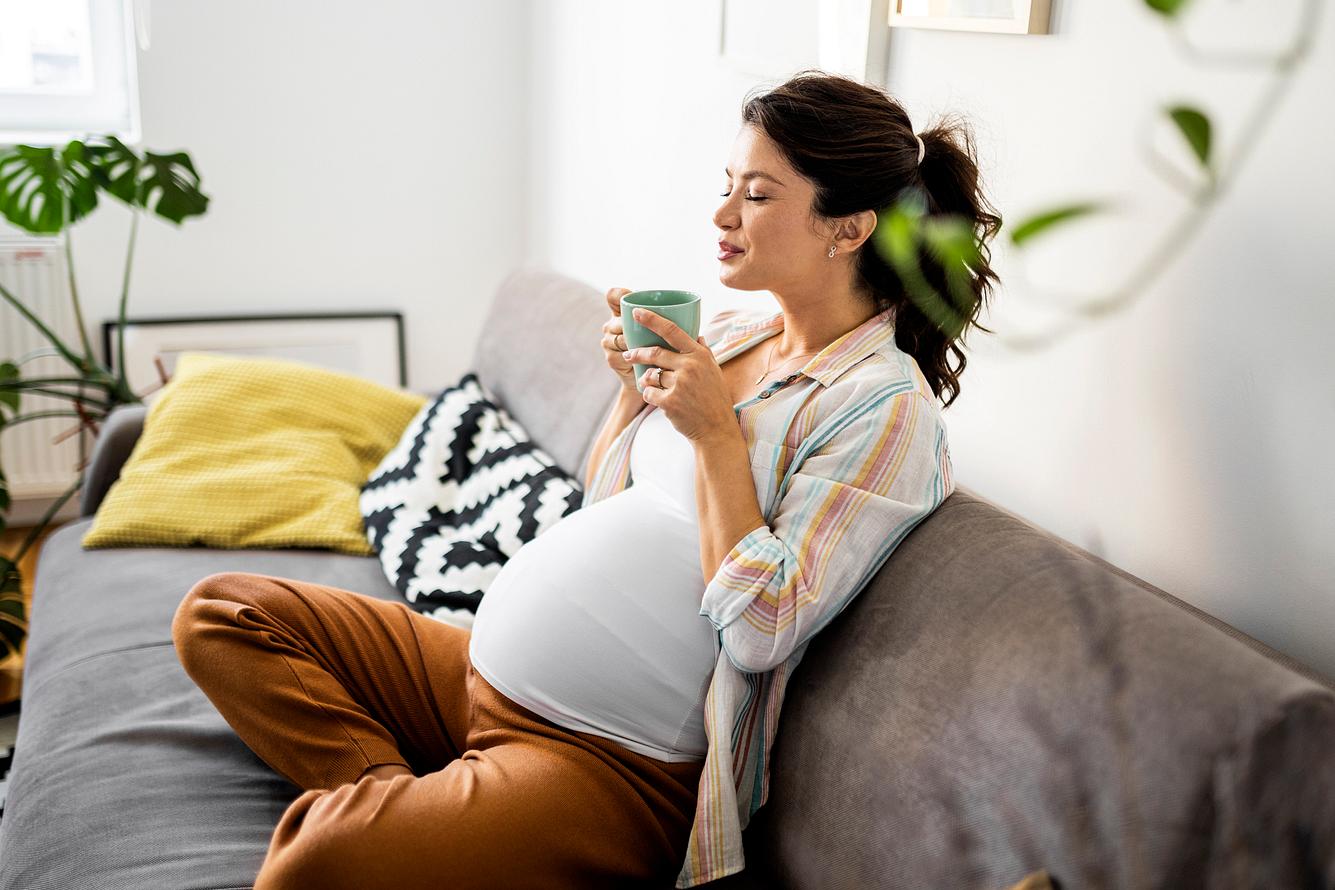 blaehungen-schwangerschaft Schwangere Frau mit Tee sitzt auf dem Sofa