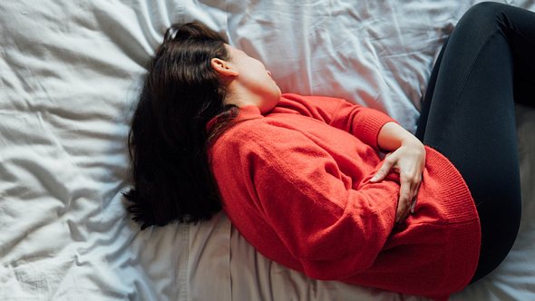 Eine Frau krümmt sich im Bett vor Schmerzen - Foto: istock_evrim ertik