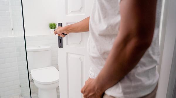 Mann öffnet Tür zur Toilette - Foto: iStock/ferlistockphoto