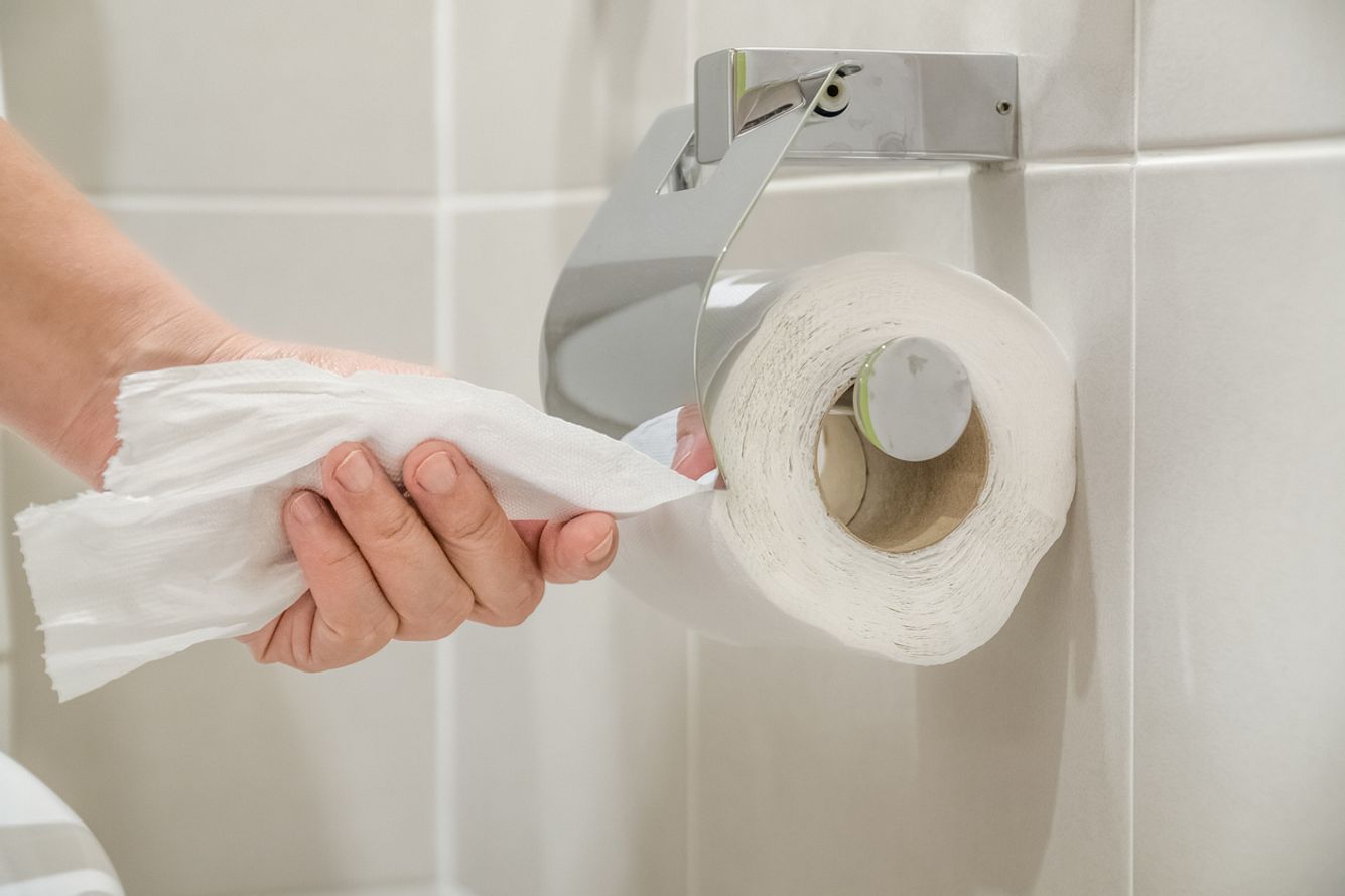 Eine Frauenhand reißt Toilettenpapier von einer Rolle im Bad