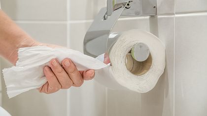 Eine Frauenhand reißt Toilettenpapier von einer Rolle im Bad - Foto: iStock-938484184 Toa55