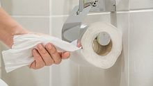 Eine Frauenhand reißt Toilettenpapier von einer Rolle im Bad - Foto: iStock-938484184 Toa55