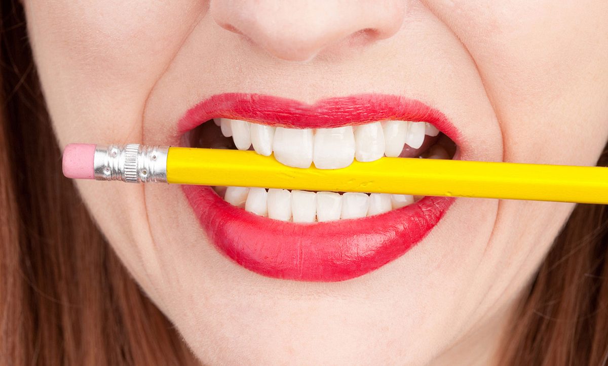 Frau hat einen Bleistift zwischen den Zähne