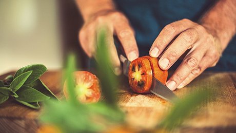 Eine Frau schneidet Tomaten auf einem Holzbrett - Foto: istock_knape