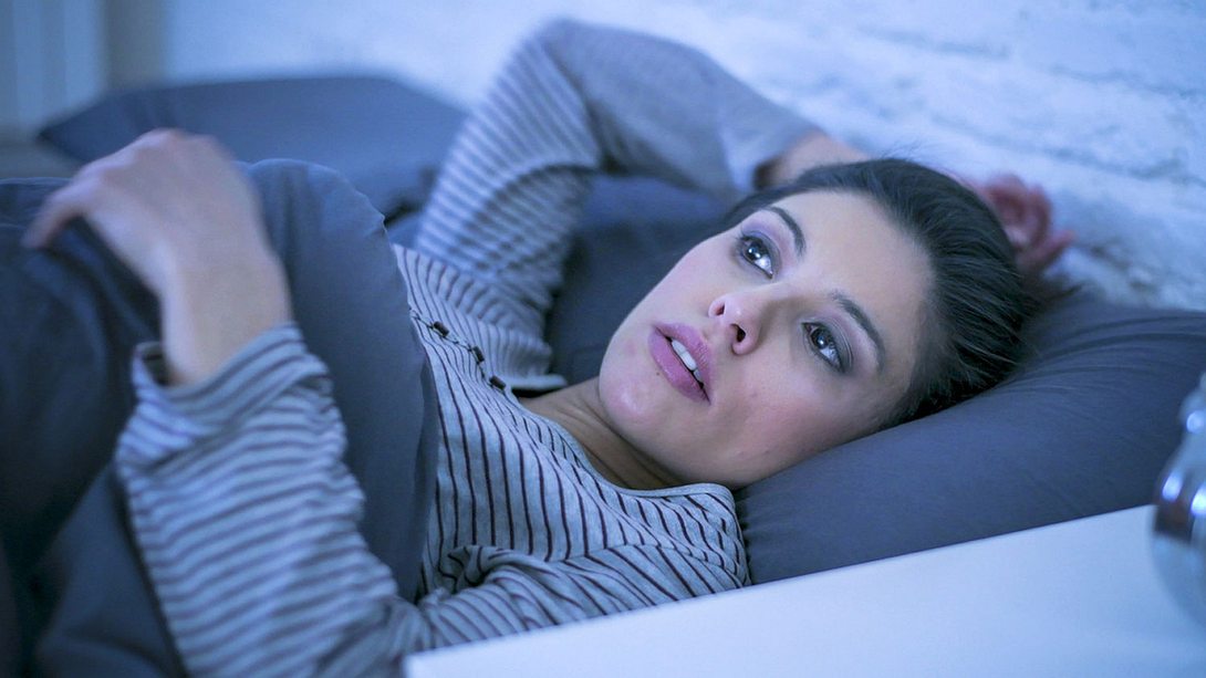 Eine Frau liegt im Bett und schaut besorgt - Foto: iStock/OcusFocus