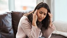 Eine Frau sitzt scheinbar irritiert auf  einer Couch und fasst sich an die Schläfen.  - Foto: iStock / PeopleImages