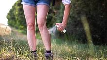 Eine Frau sprüht ihre Beine auf einer Wiese ein. - Foto: iStock / Zbynek Pospisil