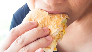 Frau beisst in Burger - Foto: iStock/sutteerug