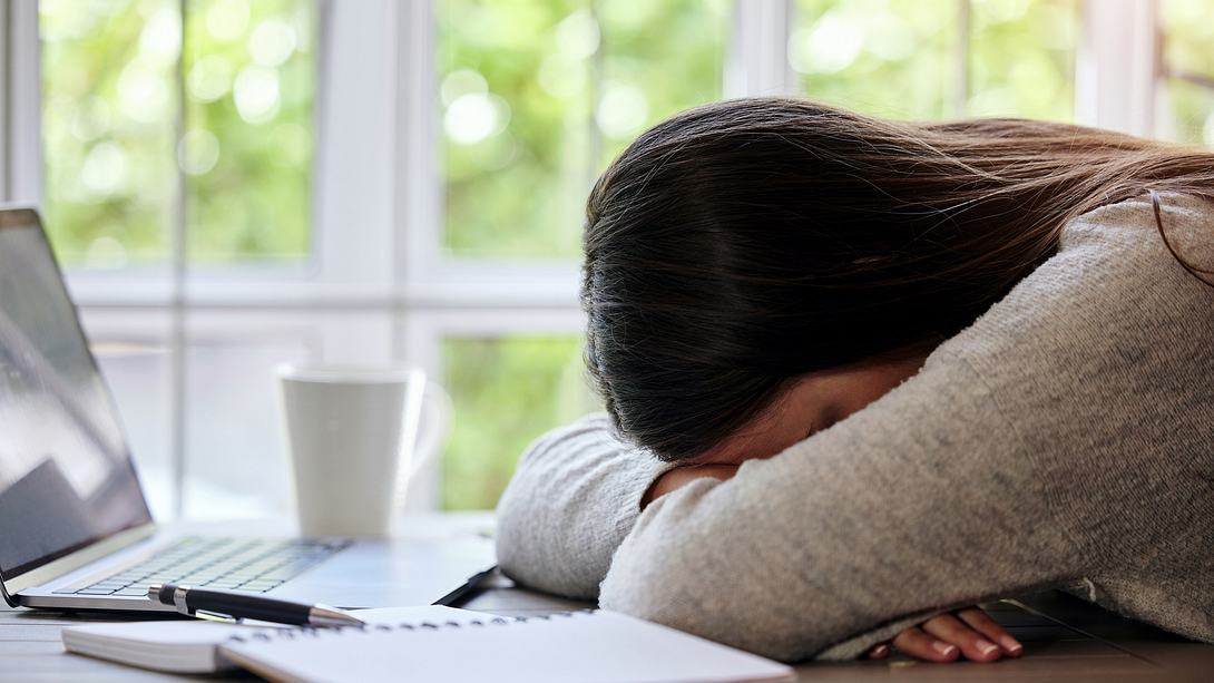 Frau mit Burnout liegt mit dem Kopf auf einem Schreibtisch - Foto: iStock/PeopleImages