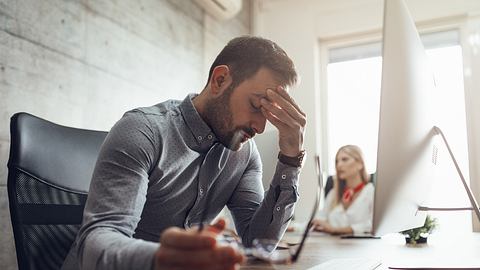 Mann vor Computer stützt erschöpft den Kopf in die Hand - Foto: iStock/MilanMarkovic