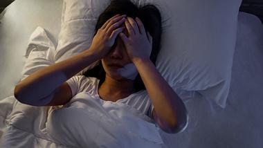 Frau liegt wach im Bett und hält sich die Hände vor die Augen - Foto: iStock/Phira Phonruewiangphing