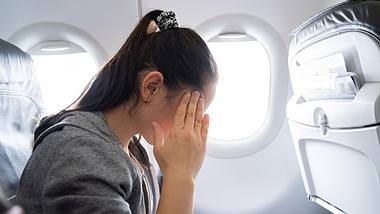 Eine Frau sitzt im Flugzeug und fasst sich an die Schläfe - Foto: istock_AndreyPopov