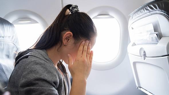 Eine Frau sitzt im Flugzeug und fasst sich an die Schläfe - Foto: istock_AndreyPopov