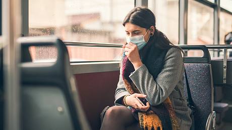 Frau mit Maske in der Bahn hustet - Foto: istock/ArtistGNDphotography