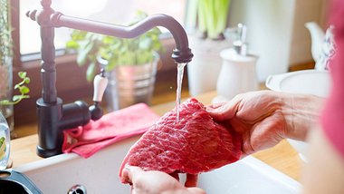 Ein Stück Fleisch wird in den Händen unter den Wasserhahn gehalten - Foto: istock_Halfpoint