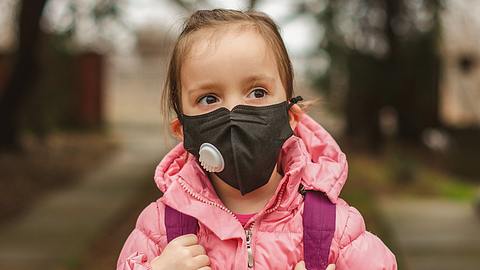 Mädchen in rosa Jacke trägt einen schwarzen Mund-Nasen-Schutz - Foto: iStock-1205547770 StockPlanets