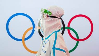 Person in Schutzkleidung steht vor Olympischen Ringen - Foto: IMAGO/Bildbyran