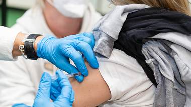 Frauenoberarm; Hände in blauen Schutzhandschuhen setzen eine Spritze - Foto: IMAGO/Fotostand