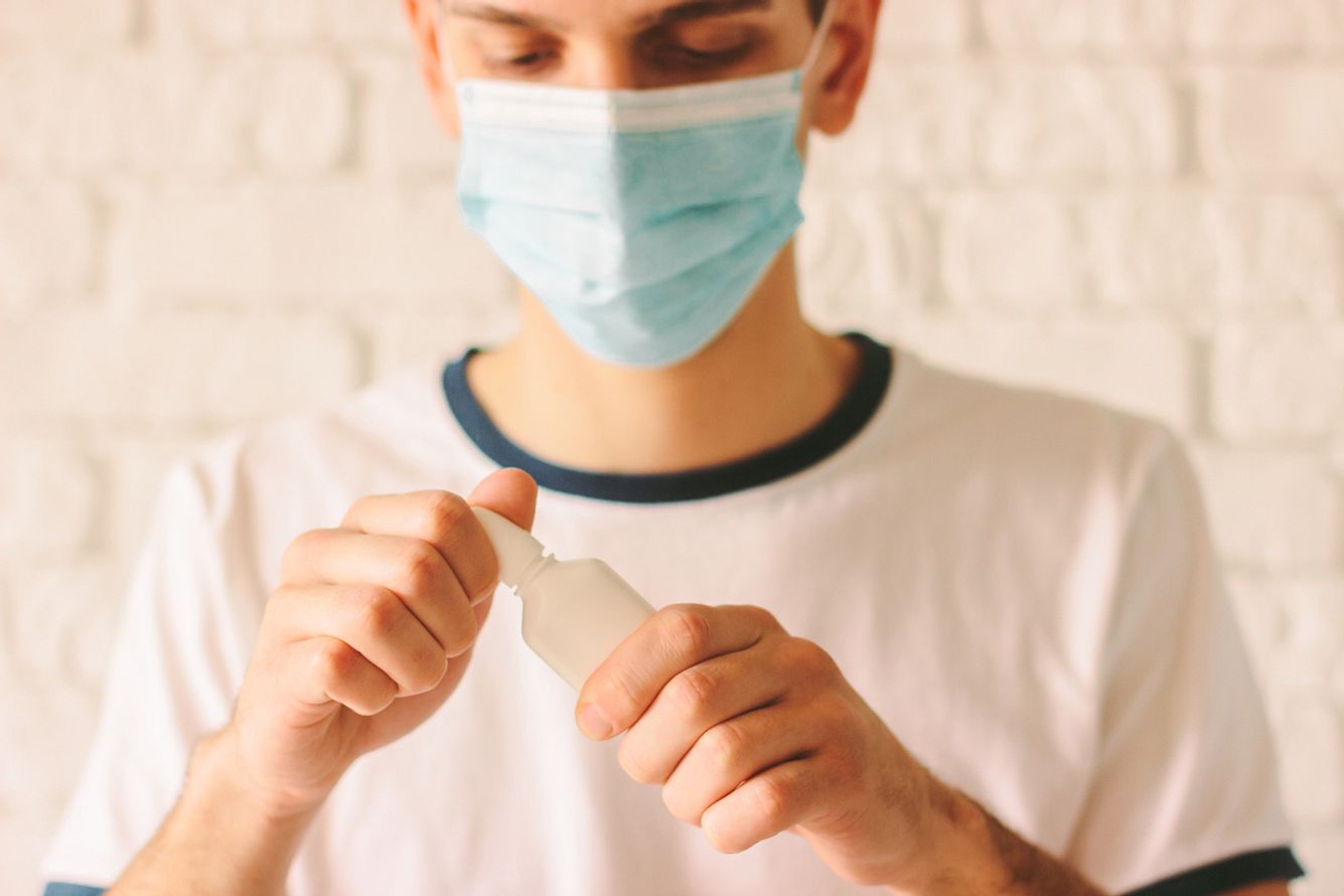 Junger Mann mit Maske hält Nasenspray in der Hand