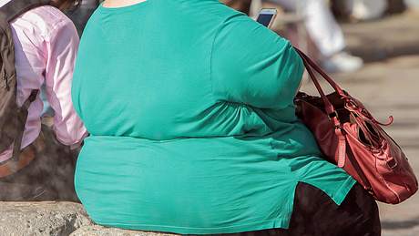 Stark übergewichtige Frau im grünen Shirt, sitzend, Rücken zur Kamera - Foto: iStock/IMAGO Ralph Peters