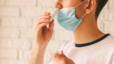 Mann mit Mundschutz, der ein Nasenspray benutzt - Foto: istock/ Artem Tryhub