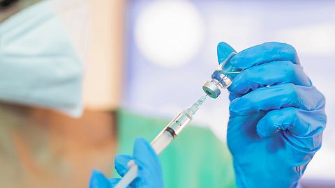 Hände in blauen Schutzhandschuhen ziehen Spritze aus einer Ampulle auf - Foto: istock / PonyWang