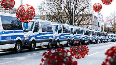 Straße mit einer Reihe von Polizei-Mannschaftswagen; Corona-Viren schweben herum - Foto: IMAGO / Michael Matthey