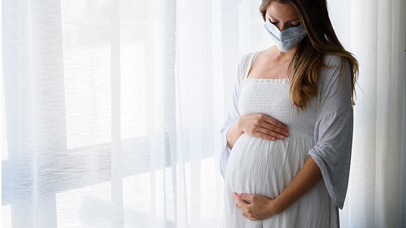 Schwangere Frau mit Maske hält sich den Bauch. - Foto: iStock/ Lordn