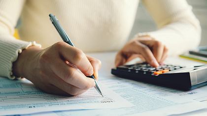 Hände einer Frau beim Ausfüllen von Steuerformularen mit Stift und Taschenrechner - Foto: iStock/pcess609