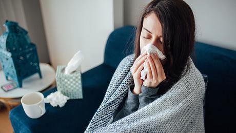 Eine Frau sitzt krank auf dem Sofa und schnäuzt ihre Nase - Foto: istock_evrim ertik