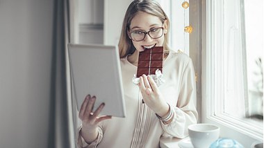 Frau mit Schokolade in der Hand vorm Bildschirm - Foto: istock/eva_katalin_kondoros