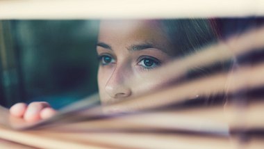 Eine Frau zieht die Rolläden vor ihrem Fenster herunter und guckt nach draußen - Foto: istock_martin-dm
