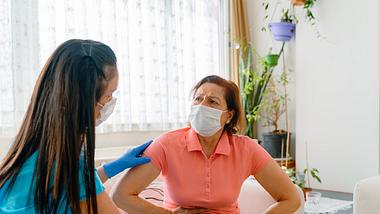 Ärztin mit Maske und Schutzhandschuhen untersucht eine Frau mit Bauchschmerzen, die ebenfalls Maske trägt - Foto: iStock-ID 1248393962 Phynart Studio