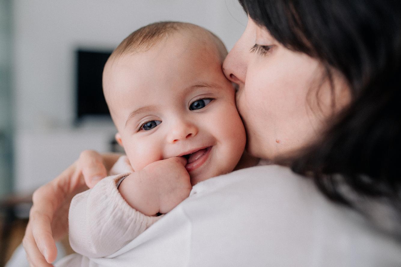 Eine Frau küsst ihr lachendes Babys auf die Wange