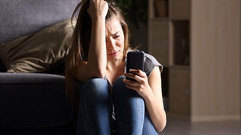 Frau schaut traurig auf ihr Handy - Foto: iStock/AntonioGuillem