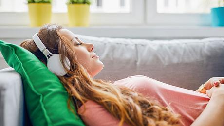 Frau mit Kopfhörern liegt auf dem Sofa - Foto:  iStock/BartekSzewczyk