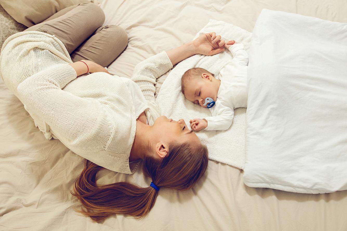 Frau schläft mit Baby im Bett