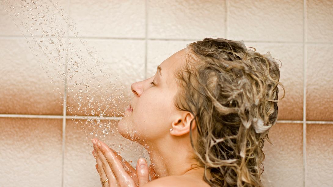 Frau steht mit shampoonierten Haaren und geschlossenen Augen unter der Dusche - Foto: iStock/kaczka