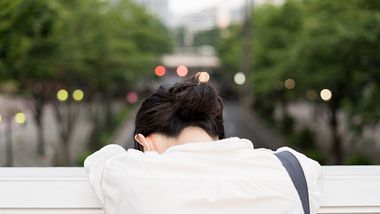 Überforderte Japanerin in einer Stadt lehnt sich erschöpft über ein Brückengeländer - Foto: iStock /AH86